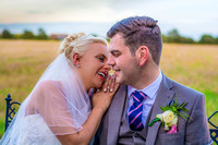 sitting on a bench the bride rests on her husband and smiles as they both look at each other